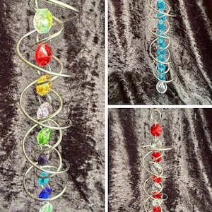 May include: Three hanging spiral ornaments made of silver-toned metal wire. One features a vertical strand of multi-coloured faceted beads, another has a strand of bright blue beads, and the third displays a strand of alternating red and clear beads.