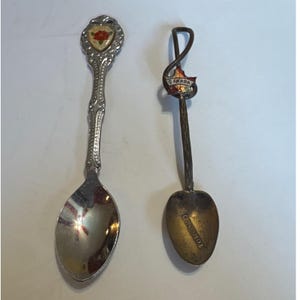 Puede incluir: Dos cucharas decorativas. Una cuchara tiene un mango plateado con un emblema floral y un cuenco plateado. La otra cuchara tiene un mango marrón con un emblema de Canadá y un cuenco dorado con la palabra "Toronto" grabada.