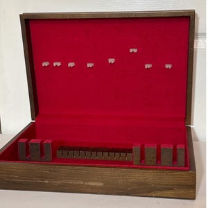 Può includere: Una scatola di legno per riporre le posate con interno in velluto rosso. La scatola è aperta, rivelando scomparti per varie utensili. L'esterno ha una finitura marrone scuro e l'interno è di un rosso vibrante. La scatola è progettata per contenere un set completo di posate.