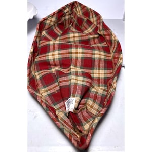 May include: A fabric head covering featuring a plaid pattern in shades of red, green, and beige. The item has a pointed shape and includes a small white rectangular tag on the interior with text that reads "MADE IN LONDON ENGLAND".