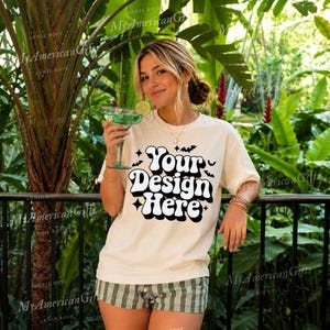 May include: A cream-coloured short-sleeve t-shirt featuring the black text Your Design Here in a bold, retro-style font, accented with small black bat and star graphics. The shirt is paired with green and white plaid shorts.