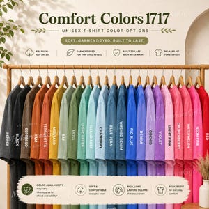 Puede incluir: Una colección de camisetas Comfort Colors 1717 colgadas en un perchero de madera, dispuestas en un degradado de colores que incluye pepper, black, espresso, yam, terracotta, mustard, bay, moss, light green, island reef, chambray, blue jean, washed denim, flo blue, denim, orchid, violet, light pink, crunchberry, watermelon, neon pink y red.