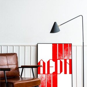 May include: A framed art print with a striking red and white design, positioned against a white wall. A brown leather armchair and a black floor lamp with a conical shade are in the foreground, creating a modern interior aesthetic.