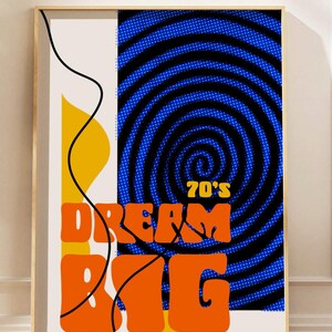 May include: A framed art print with a retro design. The artwork features the words "70's DREAM BIG" in orange, set against a blue spiral and a cream background with yellow and black accents. The print has a wooden frame.