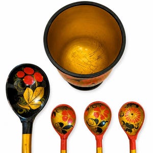 Könnte beinhalten: Ein Set aus vier Holzlöffeln und einem zylindrischen Behälter. Die Löffel zeigen schwarze, rote und goldene Blumenmuster mit langen gelben Griffen. Der Behälter hat einen schwarzen Rand, ein goldenes Inneres und ein rot-schwarzes Äußeres.