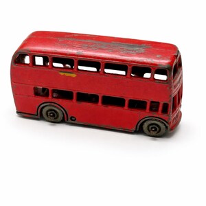 May include: A vintage red double-decker bus toy with black wheels. The toy bus has a weathered appearance, suggesting it is an antique or a well-loved item. The windows are visible, and the overall design is a classic representation of a London bus.