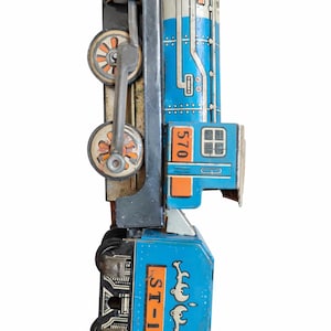 May include: Vintage blue and silver toy train with orange and white accents. The train features the number "570" and the text "ST-1" on its side. The wheels are orange and the train is made of metal.