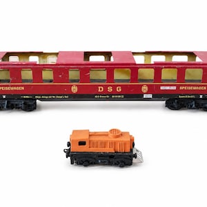 May include: A red model train dining car with yellow windows and the text DSG and SPEISEWAGEN printed on the side, accompanied by a smaller, separate orange and black model train engine component with a chimney and black wheels.