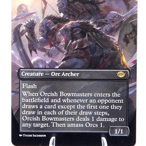 Peut inclure: Carte Magic: The Gathering "Orcish Bowmasters" avec une illustration d'Orcs au combat. Le texte de la carte inclut "Cr&eacute;ature - Archer Orc" et des instructions de jeu. La carte a une force/endurance de 1/1.