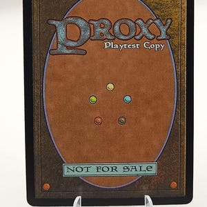 Peut inclure: Une carte &agrave; collectionner avec un fond marron et une bordure noire. La carte pr&eacute;sente le mot "DROXY" dans une police stylis&eacute;e, avec "Playtest Copy" en dessous. Le bas de la carte indique "NOT FOR SALE".