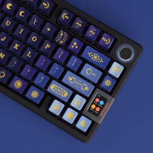 May include: A black mechanical keyboard with blue and purple keycaps. The keycaps feature celestial designs in gold and white, including moons, suns, and stars. The keyboard has a small screen and the word "INFVERSE" is printed on the side.