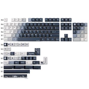 May include: A set of keycaps in various sizes and shapes, designed for a mechanical keyboard. The keycaps are primarily white, gray, and dark blue. Some keycaps have text and symbols printed on them, including letters, numbers, and special characters.