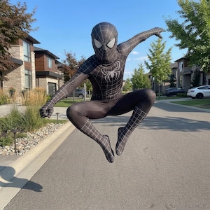 May include: A black and white Spider-Man costume with a spider emblem on the chest and a web pattern. The costume is worn by a person jumping in the air on a residential street.
