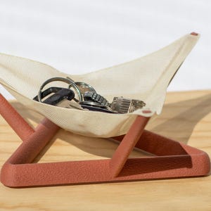 Könnte beinhalten: Ein moderner Schlüsselhalter mit einer Leinenschlinge, die von einem terracottafarbenen Rahmen gehalten wird. Die Schlinge enthält mehrere Schlüssel und Schlüsselanhänger. Das Design ist minimalistisch und funktional, geeignet für einen Eingangsbereich oder Schreibtisch.