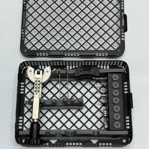 May include: An open black surgical instrument tray with a grid pattern, holding various surgical tools. The tray contains a wrench, screws, and other medical devices. The text "MEDI" is visible.
