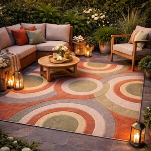 May include: Outdoor patio scene with a large area rug featuring concentric circles in shades of orange, green, gray, and cream. The patio includes a sectional sofa, wooden chairs, a coffee table, and string lights.