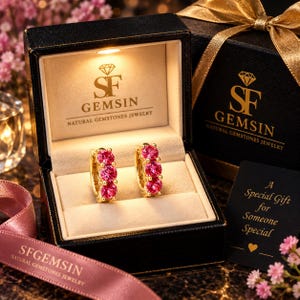 Puede incluir: Un par de pendientes de aro dorados con tres piedras preciosas rosas redondas cada uno, presentados en un joyero negro con luz interna. La tapa muestra el logotipo de SF GEMSIN y una tarjeta dice A Special Gift for Someone Special.