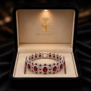 Può includere: Un bracciale color argento con gemme rosse dal taglio ovale circondate da piccole pietre trasparenti in un'incastonatura in filigrana. Il bracciale è esposto all'interno di un portagioie in velluto nero con il testo dorato SF GEMS IN stampato.