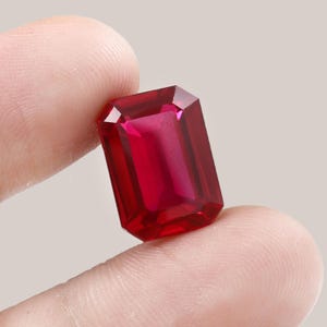 Peut inclure: Une pierre précieuse rouge vif et profonde taillée en forme d'émeraude rectangulaire avec des bords facettés. La pierre présente une grande clarté et une teinte cramoisie riche et saturée, reflétant la lumière sur ses surfaces polies.