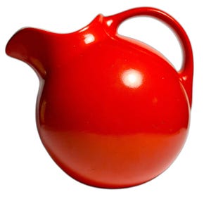 May include: A bright red ceramic pitcher with a spherical body, a curved handle on the right side, and a wide pouring spout on the left. The surface has a smooth, glossy finish that reflects light, creating a uniform and vibrant appearance.
