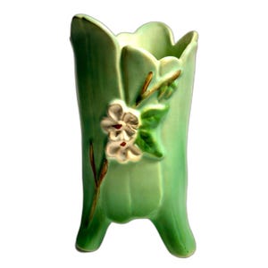 May include: A light green ceramic vase with a scalloped rim and three feet. The exterior features a raised relief design of white flowers with dark centers and brown stems with green leaves, applied to the front of the smooth, glossy surface.