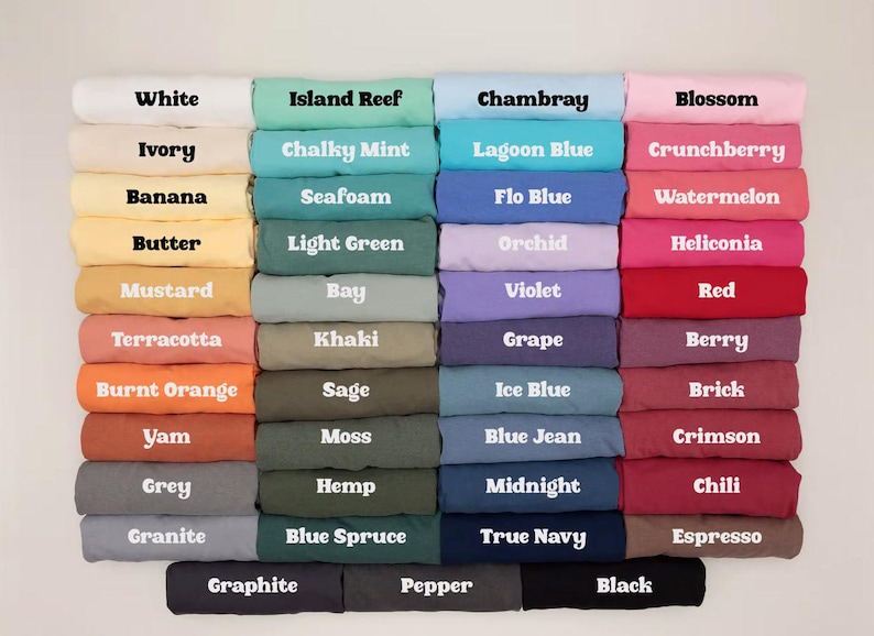 May include: A grid of folded t-shirts in various colours, each labelled with its specific colour name in white or black text. The collection includes shades of white, yellow, orange, red, pink, purple, blue, green, grey, brown, and black.