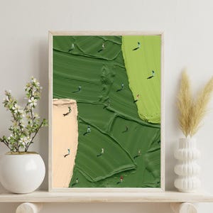May include: Abstract art print depicting a textured green and beige landscape with miniature figures. The artwork is framed in a light wood frame, creating a sense of depth. The painting is displayed on a white shelf with decorative vases, adding to the aesthetic.