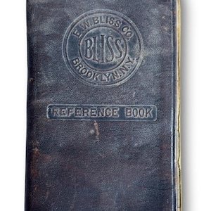 Könnte beinhalten: Ein dunkelbraunes, ledergebundenes Referenzbuch im Vintage-Stil. Der Einband zeigt geprägten Text und ein rundes Logo mit der Aufschrift "E.W. Bliss Co. Bliss Brooklyn, N.Y.". Der Titel "REFERENCE BOOK" ist ebenfalls geprägt. Das Buch weist Gebrauchsspuren auf.