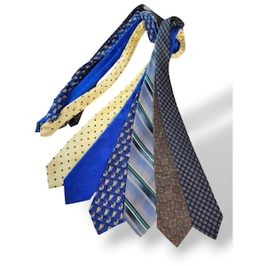 May include: A collection of six neckties displayed in a fan shape. The ties feature various patterns including black polka dots on cream, solid blue, blue with small geometric shapes, blue and grey diagonal stripes, brown with diamond motifs, and navy.
