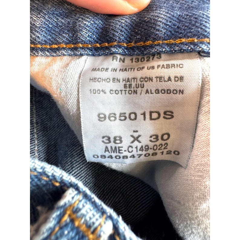 May include: Close-up of a blue denim jeans label. The label includes the RN number 130273, size 38 x 30 inches, and the text "MADE IN HAITI OF US FABRIC". The jeans are 100% cotton.