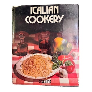 May include: A hardcover cookbook titled Italian Cookery with a black cover featuring a white plate of spaghetti, a glass of red wine, a glass cruet, a yellow bell pepper, red tomatoes, and garlic cloves on a red and white checkered tablecloth.