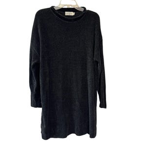 May include: A long-sleeved, charcoal black sweater featuring a textured, waffle-knit pattern throughout. The garment has a high, rounded neckline and a straight hemline, presented on a clear plastic hanger against a plain white background.