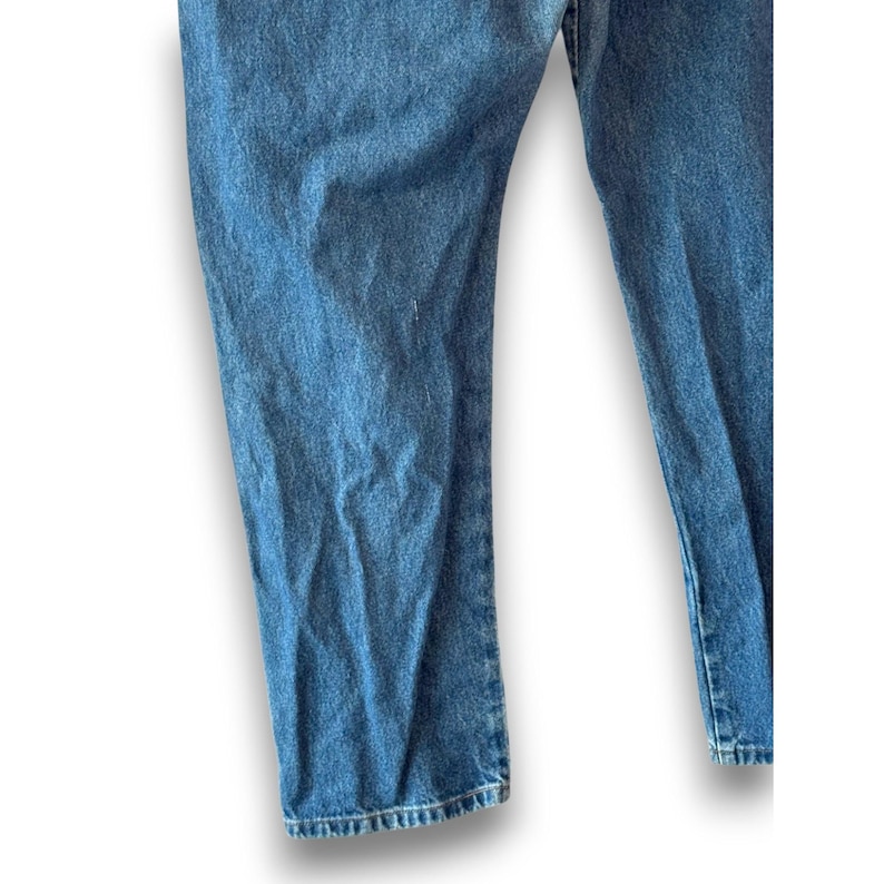May include: Close-up of light blue denim jeans. The jeans have a classic, straight-leg fit and a medium wash. The fabric shows subtle fading and wear, suggesting a vintage or well-loved appearance. The image highlights the texture and color of the denim.