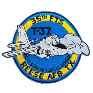 May include: Embroidered patch with a blue background and yellow border. The patch features a white T-37 jet with a cartoon face and the text "35th FTS T-37 REESE AFB TX." The text "DO IT SLOW AND SHE'LL SCREAM" is also included.