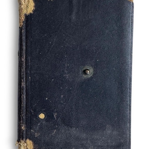 May include: A vintage, rectangular book with a dark blue leather cover. The corners and edges show wear and tear, with exposed, aged paper. A small, metal clasp is centered on the front cover. The book's overall appearance suggests age and use.