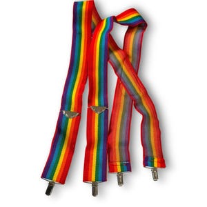 Puede incluir: Tirantes de arcoíris con clips de metal plateado. Los tirantes presentan un vibrante espectro de colores, incluyendo rayas rojas, naranjas, amarillas, verdes, azules y moradas. Un accesorio colorido.