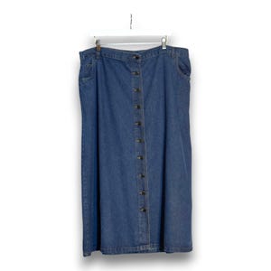 May include: A blue denim skirt with a button-down front, hanging on a white hanger. The skirt has a classic design with pockets and a button closure. The skirt is made of a medium-wash denim fabric.