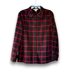 May include: A black and red plaid button-down shirt with long sleeves. The shirt has a collared neckline and is hanging on a white hanger. The plaid pattern is a classic design, suitable for casual wear.