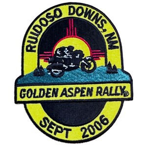 May include: An embroidered patch featuring a black motorcycle silhouette against a yellow sun and red horizon. The border is yellow with black text reading RUIDOSO DOWNS, NM, GOLDEN ASPEN RALLY, and SEPT 2006. The design includes a teal landscape base.