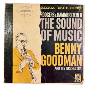 May include: Vintage vinyl record album cover for "The Sound of Music" featuring Benny Goodman and his orchestra. The cover has a black and yellow design with an illustration of a man playing a clarinet. The album is labeled "MGM STEREO".