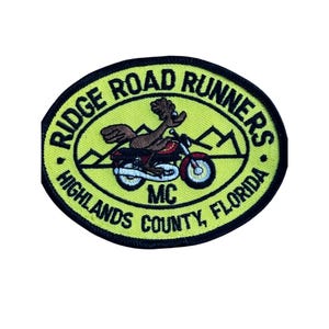 May include: An oval-shaped embroidered patch with a bright yellow background and a black border. It features a brown bird riding a red and black motorcycle, with black mountain outlines. Text reads RIDGE ROAD RUNNERS MC HIGHLANDS COUNTY, FLORIDA.