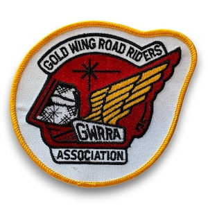 Könnte beinhalten: Gestickter Aufnäher mit weißem Hintergrund und gelbem Rand. Der Aufnäher zeigt den Text "GOLD WING ROAD RIDERS" in einer geschwungenen schwarzen Schrift. Ein rotes Flügeldesign mit gelben Akzenten und der Text "GWRRA ASSOCIATION" sind ebenfalls sichtbar.