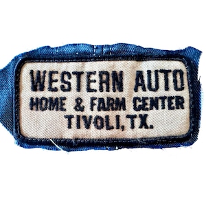 May include: A rectangular patch with the text "WESTERN AUTO HOME & FARM CENTER TIVOLI, TX." embroidered in black on a tan background. The patch is framed by a dark blue border and attached to a piece of blue denim fabric.