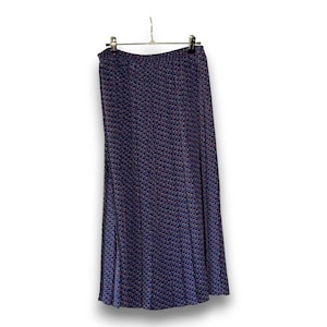 May include: A long, navy blue skirt with a woven pattern of small red, white, and blue squares. The skirt is hanging on a metal hanger against a white background. The skirt has a slight A-line shape.