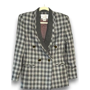 May include: A gray and white plaid blazer with a double-breasted design. The blazer has a notched lapel and gold-colored buttons. The label reads "PETITE". The blazer is hanging on a white hanger.