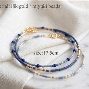 May include: Two delicate bracelets made of 18k gold and Miyuki beads in shades of blue, white, and gold. The bracelets feature a repeating pattern of small beads and measure 17.5 cm in length. Each bracelet includes a small gold circular clasp.