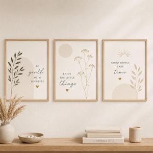 Op de afbeelding: Drie ingelijste wandkunstprints met lichtbeige achtergronden. De eerste toont een bladtak en de tekst BE GENTLE WITH YOURSELF. De tweede toont een bloemstengel en de tekst ENJOY THE LITTLE THINGS. De derde toont een zon en bladtak met de tekst GOOD THINGS TAKE TIME.