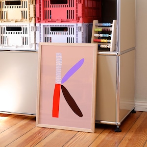 Puede incluir: Una impresión artística enmarcada con una gran letra "K" estilizada en formas abstractas. La obra de arte incluye una sección vertical con un patrón texturizado, una forma roja, una forma marrón y una forma púrpura sobre un fondo rosa claro. El marco es de madera clara.