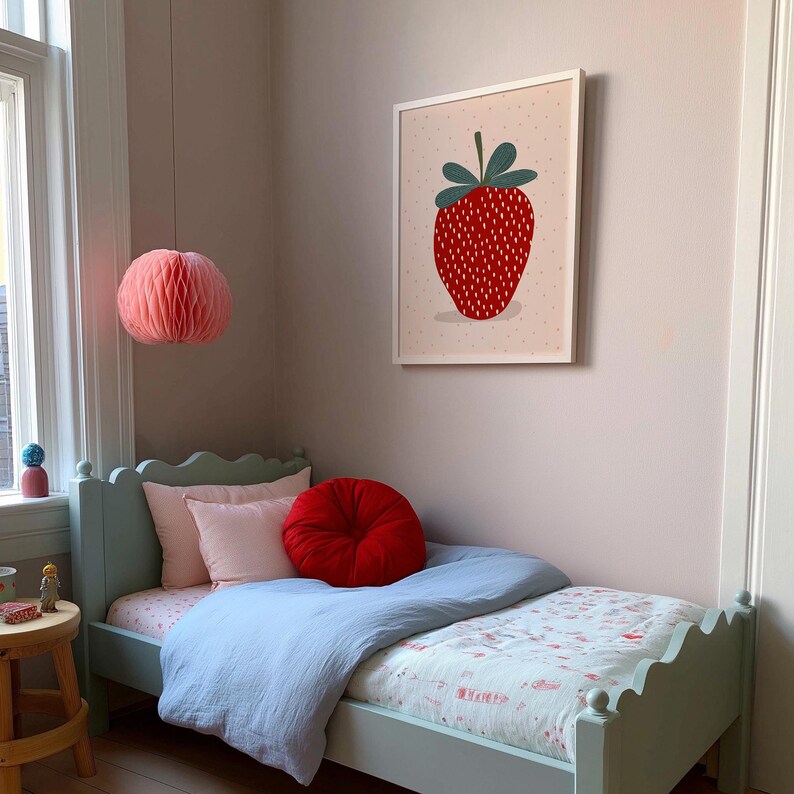 May include: A child's bedroom with a light blue bed, pink pillows, and a red round cushion. A framed strawberry art print hangs on the wall. A pink paper lantern hangs from the ceiling. The bed has a light blue duvet.