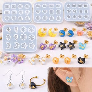 May include: An assortment of handmade earrings in various shapes and colors, including moons, hearts, stars, and butterflies. The earrings are displayed alongside silicone molds for crafting. Some earrings have gold accents.